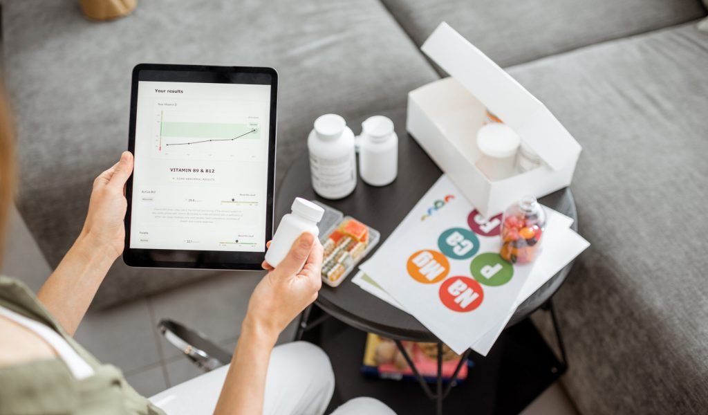 Woman checking the result of medical tests on a digital tablet, close-up with nutritional supplements on the background. Concept of individual online selection of food supplements